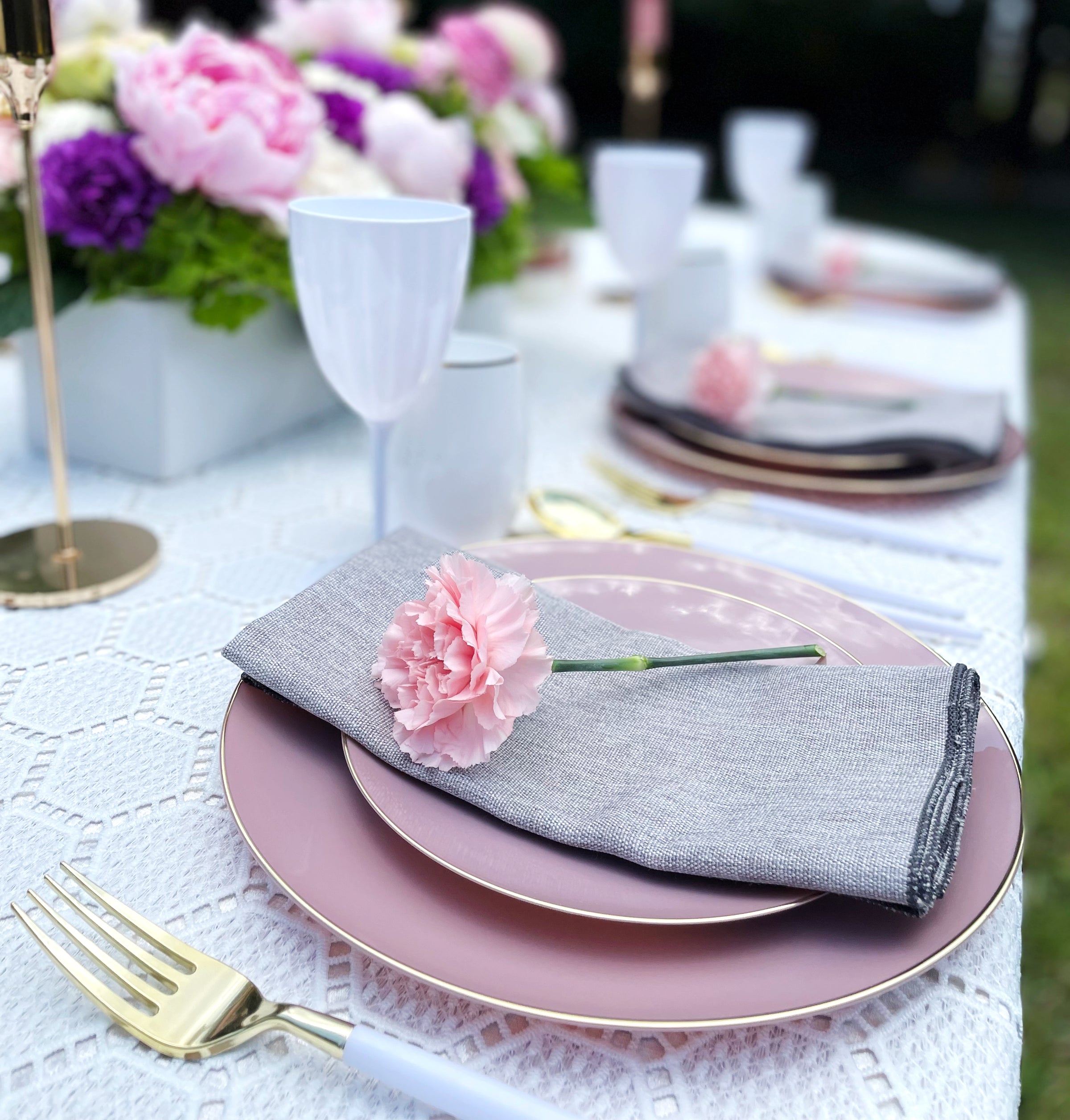 Dining table with a floral centerpiece in an outdoor scene with focus on a single place setting